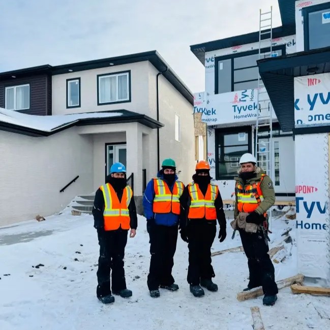 Exterior construction crew in safety gear standing in front of a house under renovation in winter.